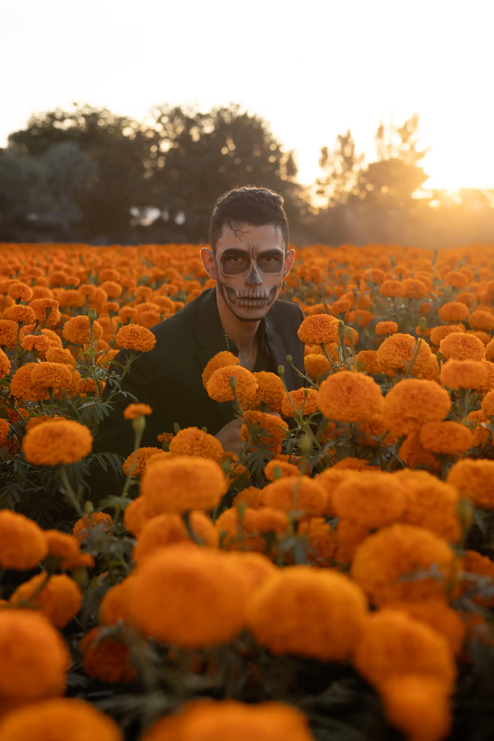 Hombre con maquillaje de catrín entre flores de cempasúchil al atardecer